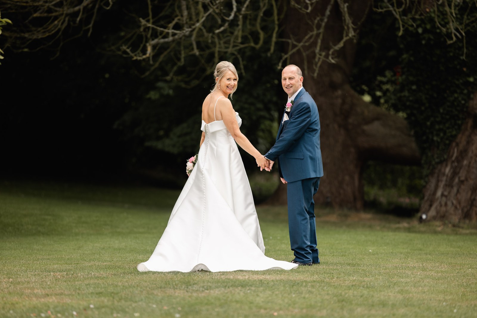 Bride and groom holding hands on the lawn beneath Glenfall House's grand old tree