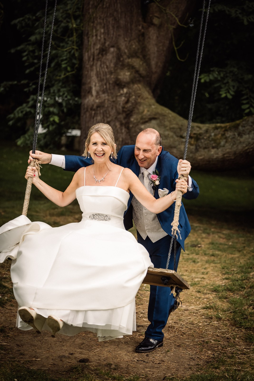 Groom pushing the bride on the garden rope swing under the old tree