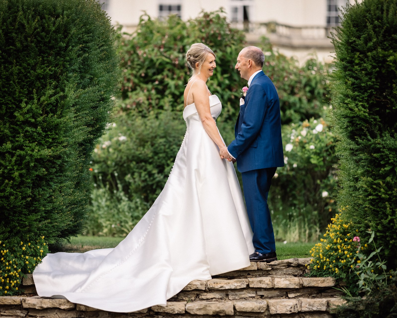 Bride and groom facing each other in the rose garden, her gown's train fanned out