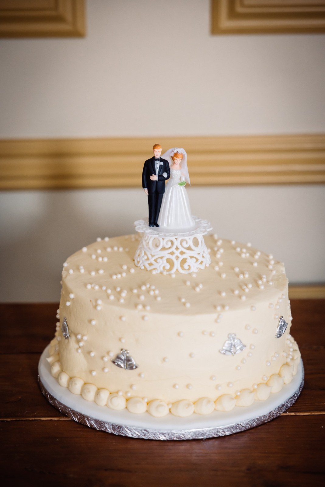 Single-tier ivory wedding cake with a bride-and-groom topper on a wooden table