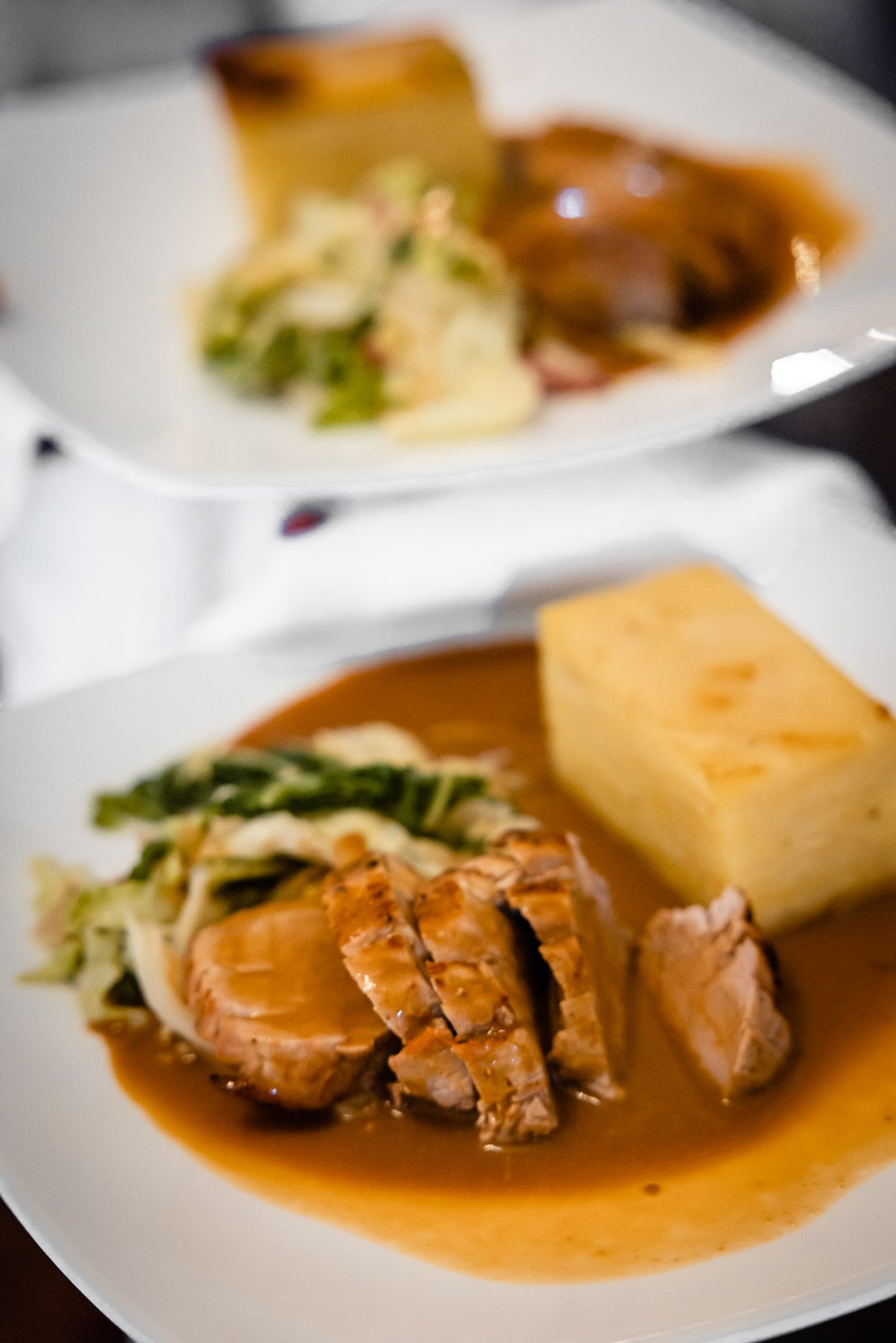 Plated wedding breakfast main course of sliced pork with vegetables and a gratin