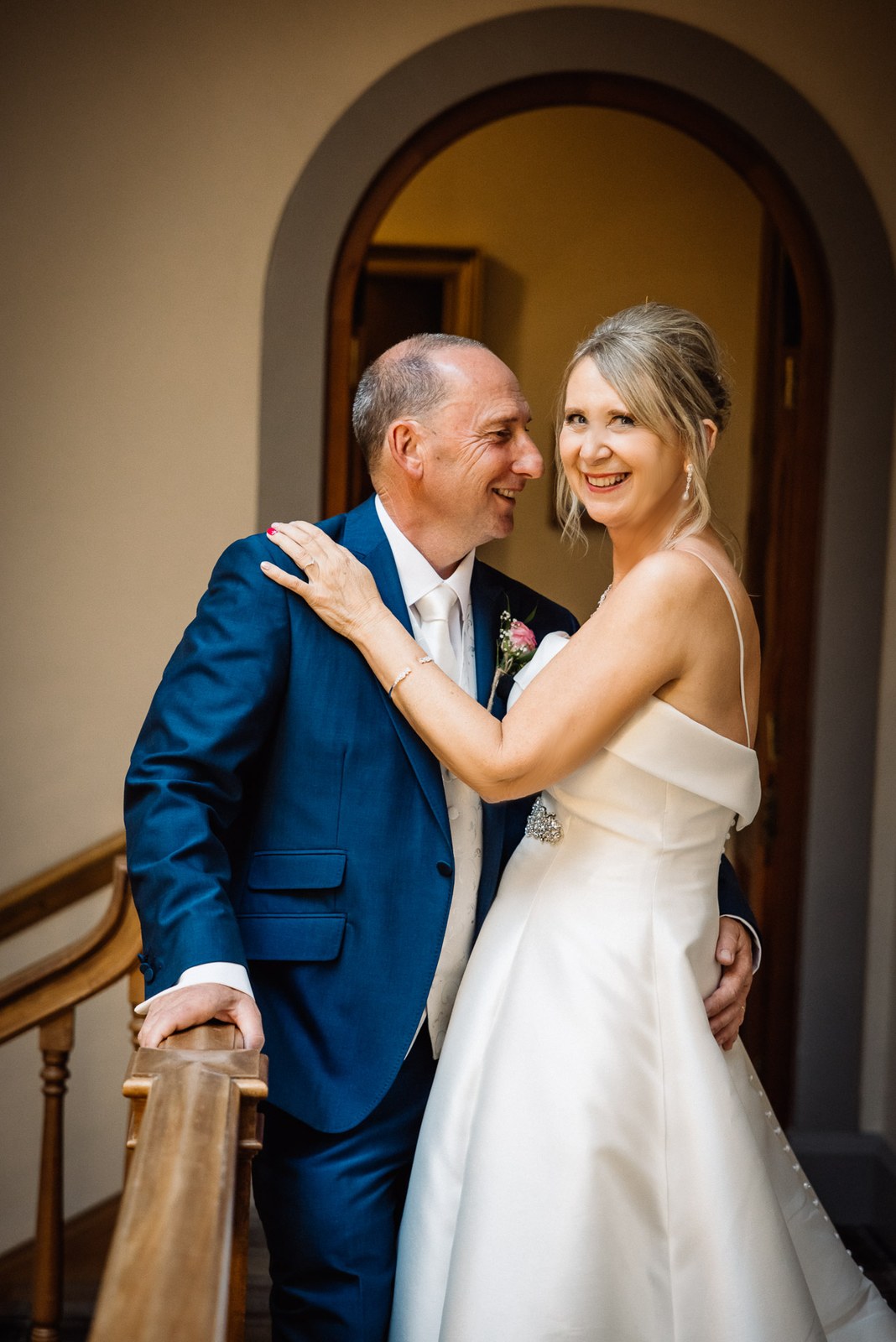 Bride and groom on the sweeping wooden staircase, laughing together