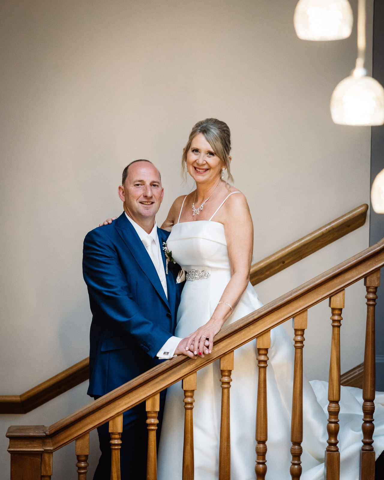 Bride and groom posing on the polished wooden staircase at Glenfall House