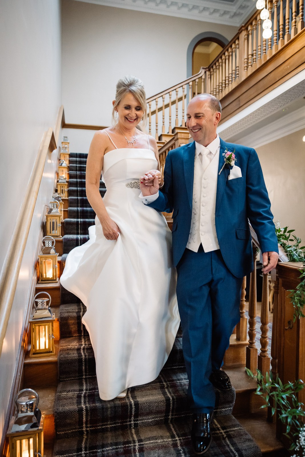 Bride and groom coming down the lantern-lit staircase with its tartan runner