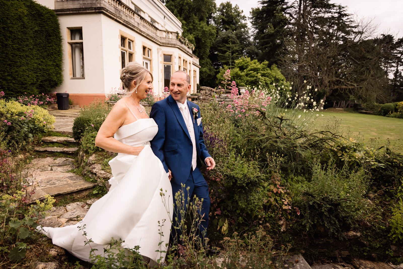 Bride and groom walking arm in arm through the garden borders beside the manor