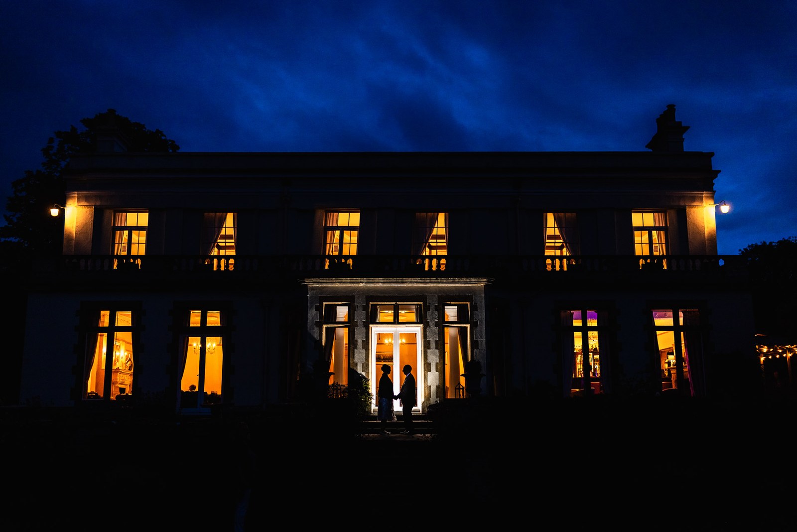 Glenfall House lit up at dusk with the couple silhouetted in the glowing doorway
