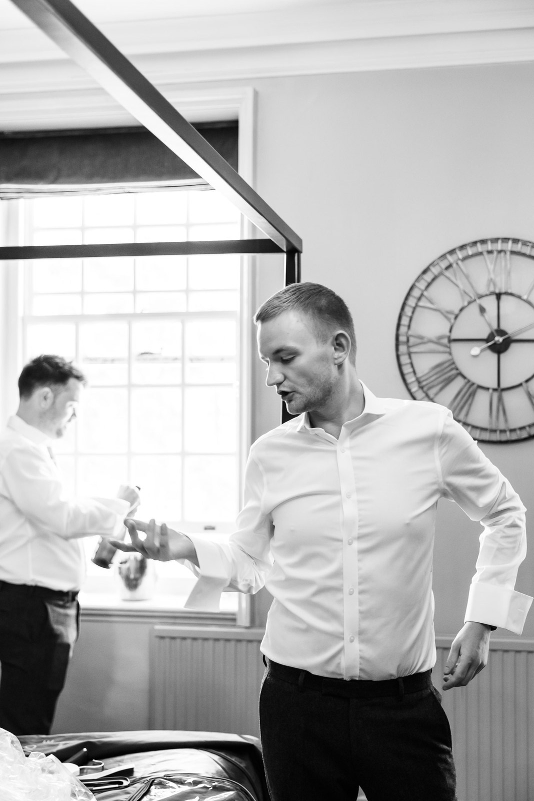 Black and white shot of a groom getting ready as a bottle is opened by the window