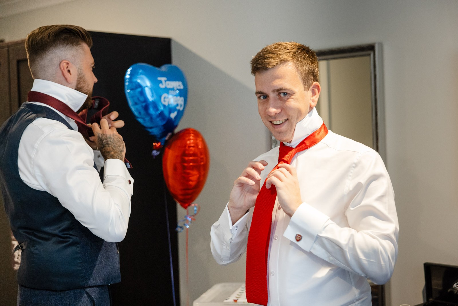 A member of the wedding party adjusting his red tie with heart-shaped balloons behind