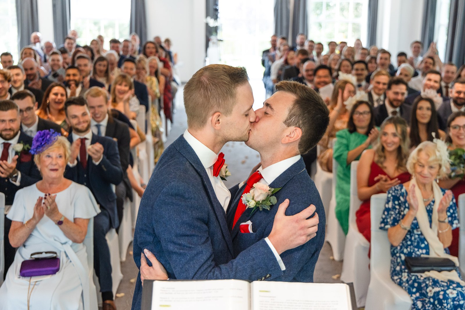 The two grooms share their first kiss as guests applaud around them