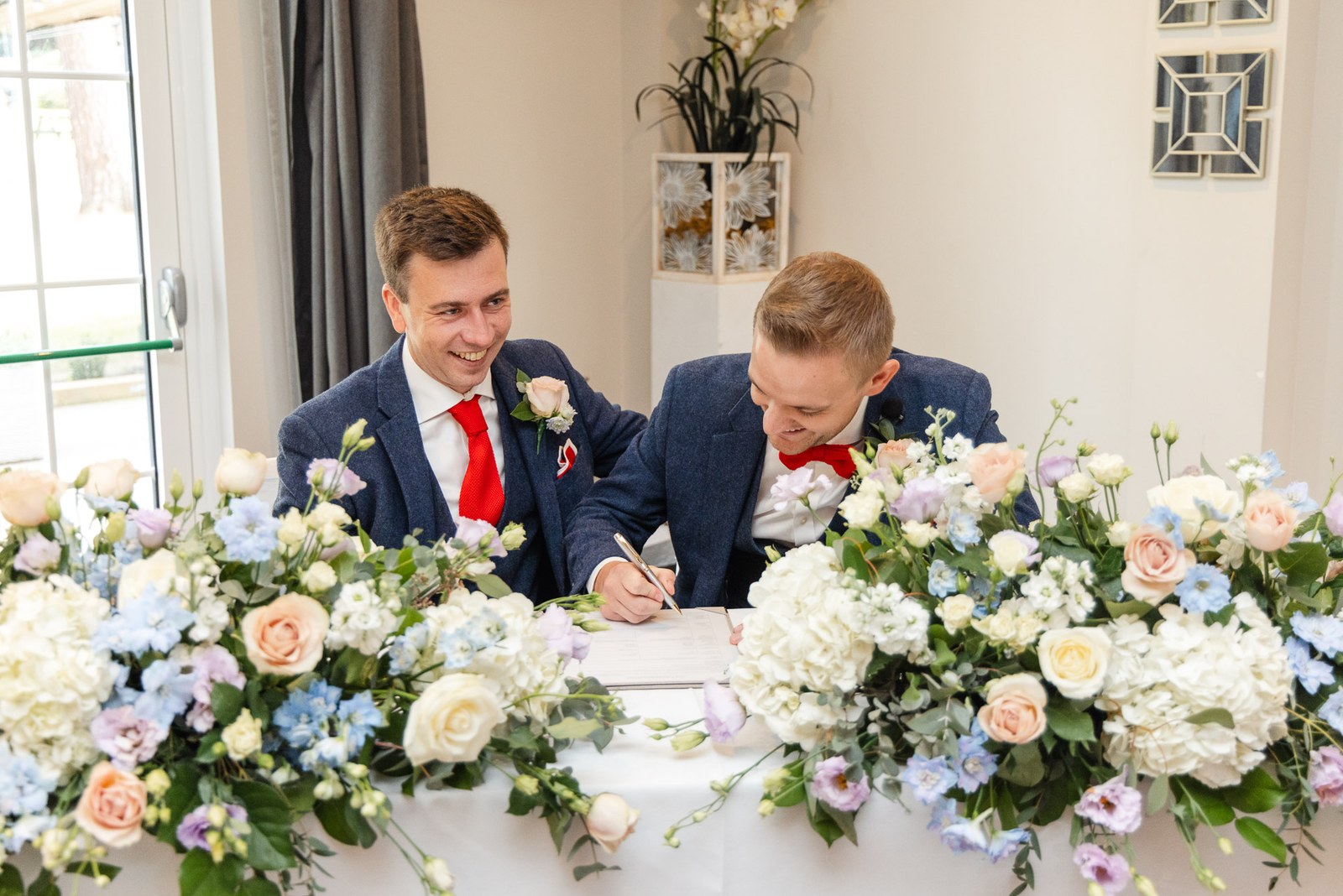 The grooms signing the register at a table dressed with pastel flowers