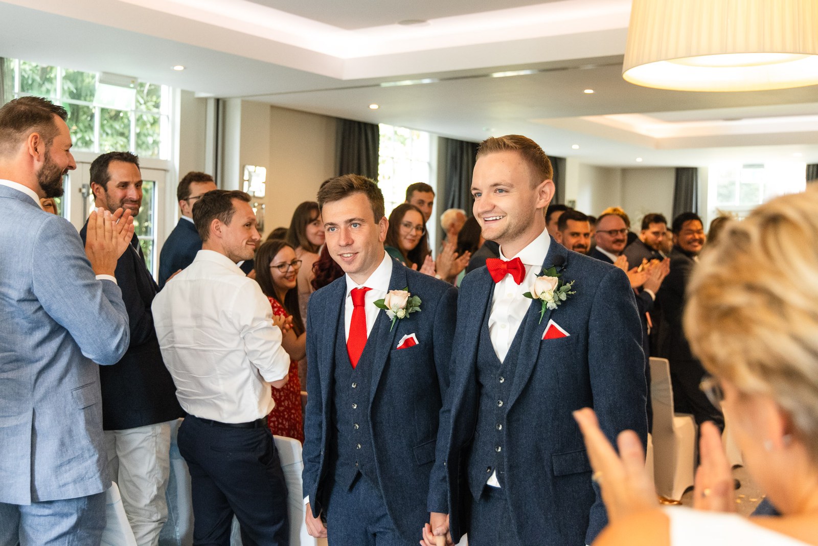The grooms hand in hand in the aisle as guests stand and applaud