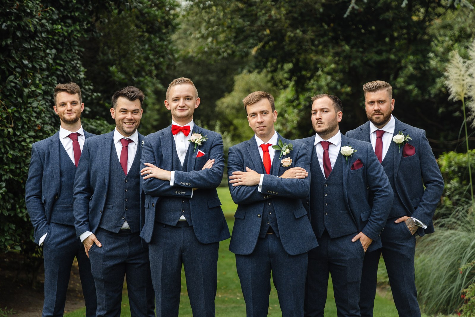 The grooms and their groomsmen in navy suits posing in the gardens of Gorse Hill Hotel