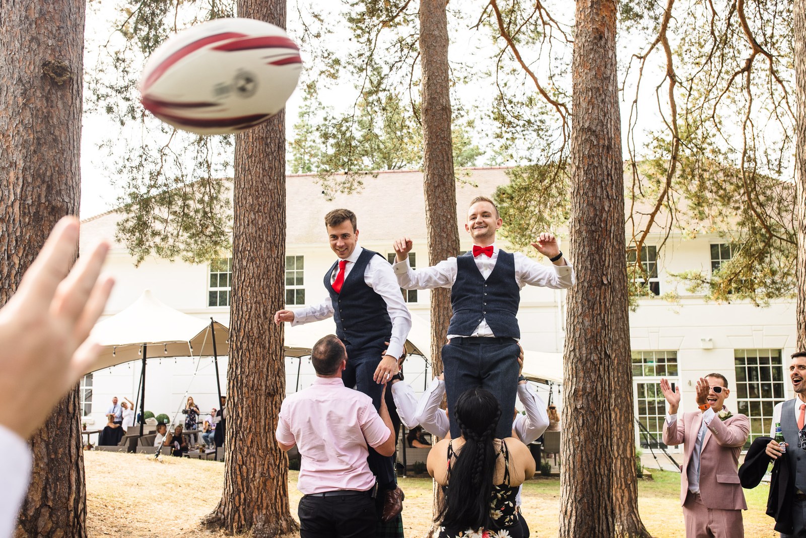 The grooms throwing a rugby ball among the tall pines outside Gorse Hill Hotel