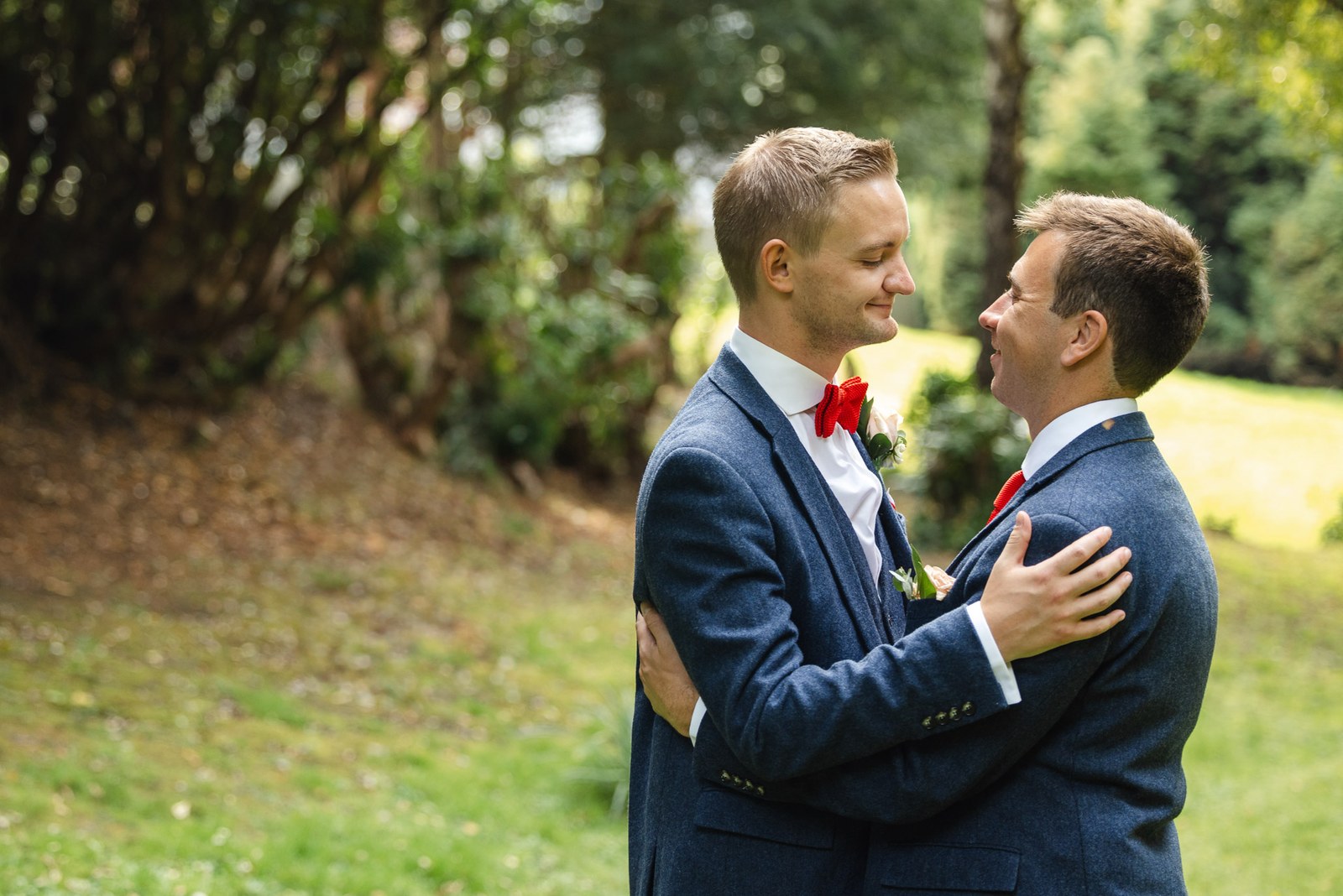 The two grooms embracing on a grassy bank beneath the trees