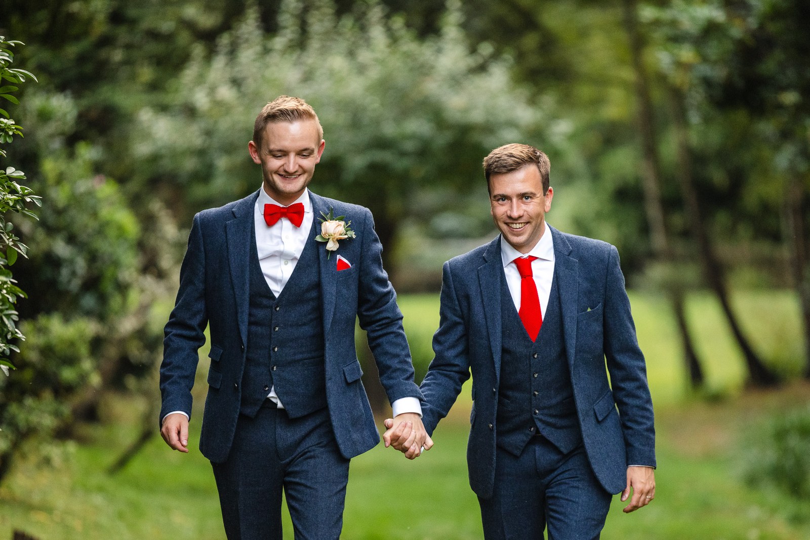 The grooms holding hands as they stroll through the wooded grounds