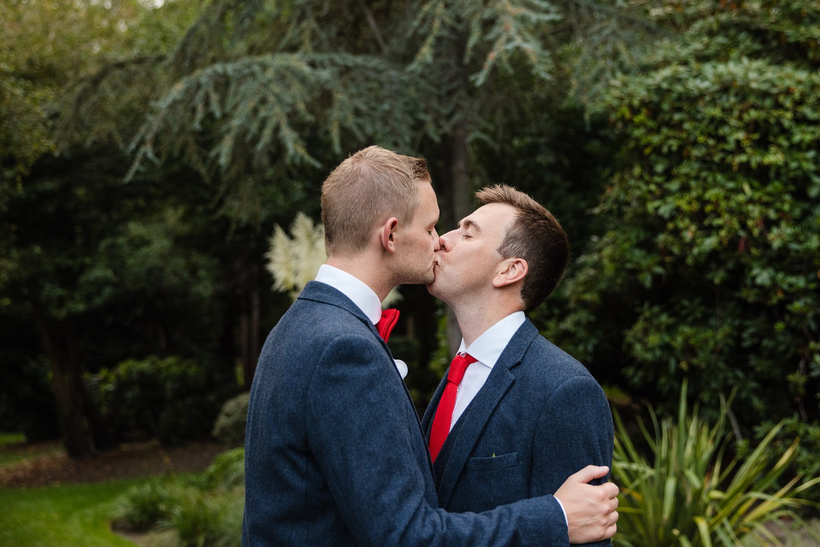 The two grooms sharing a kiss among the greenery of the gardens