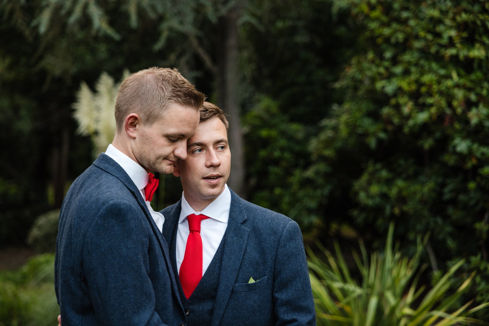 The grooms cheek to cheek surrounded by lush foliage