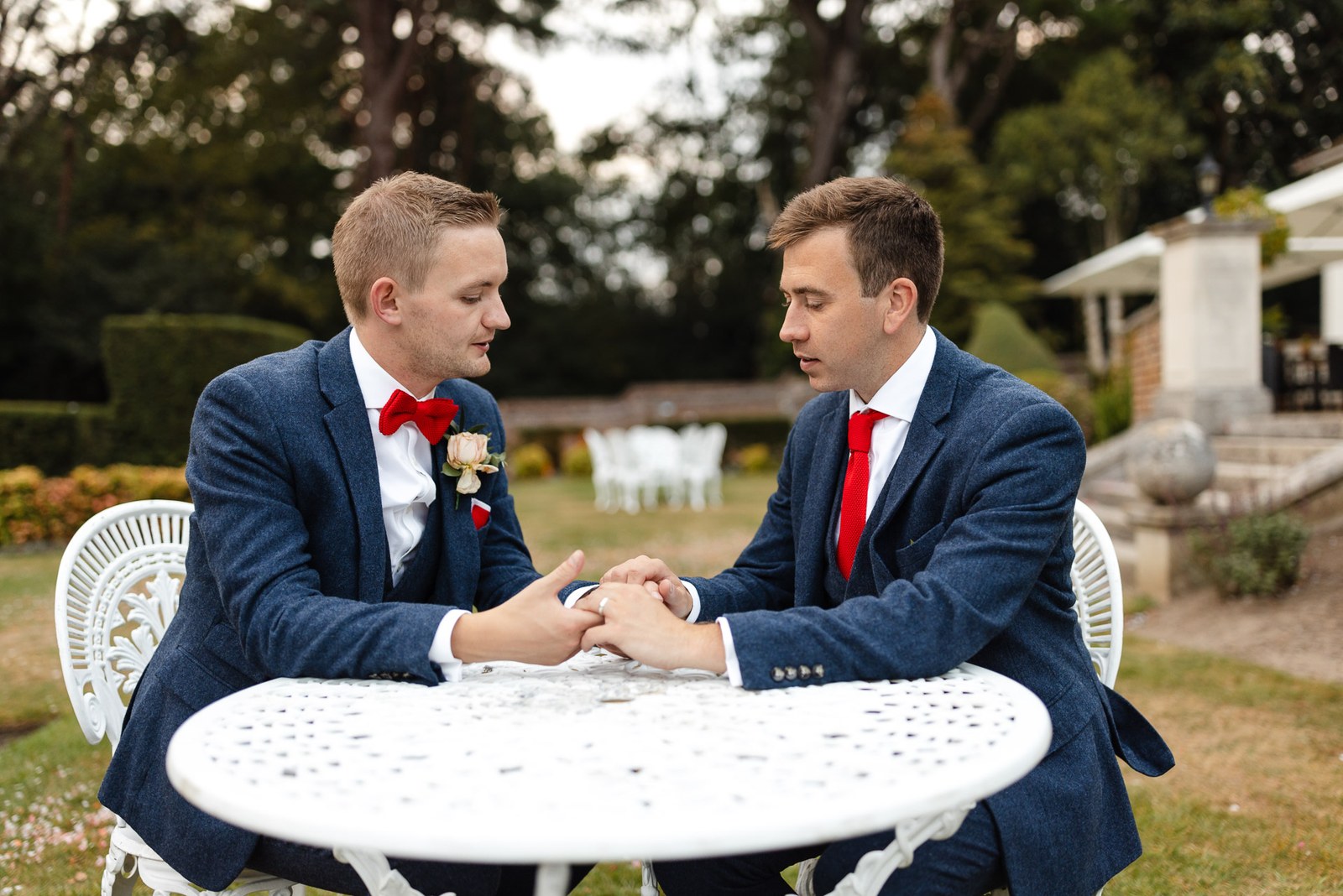 The two grooms holding hands across a white garden table in the grounds