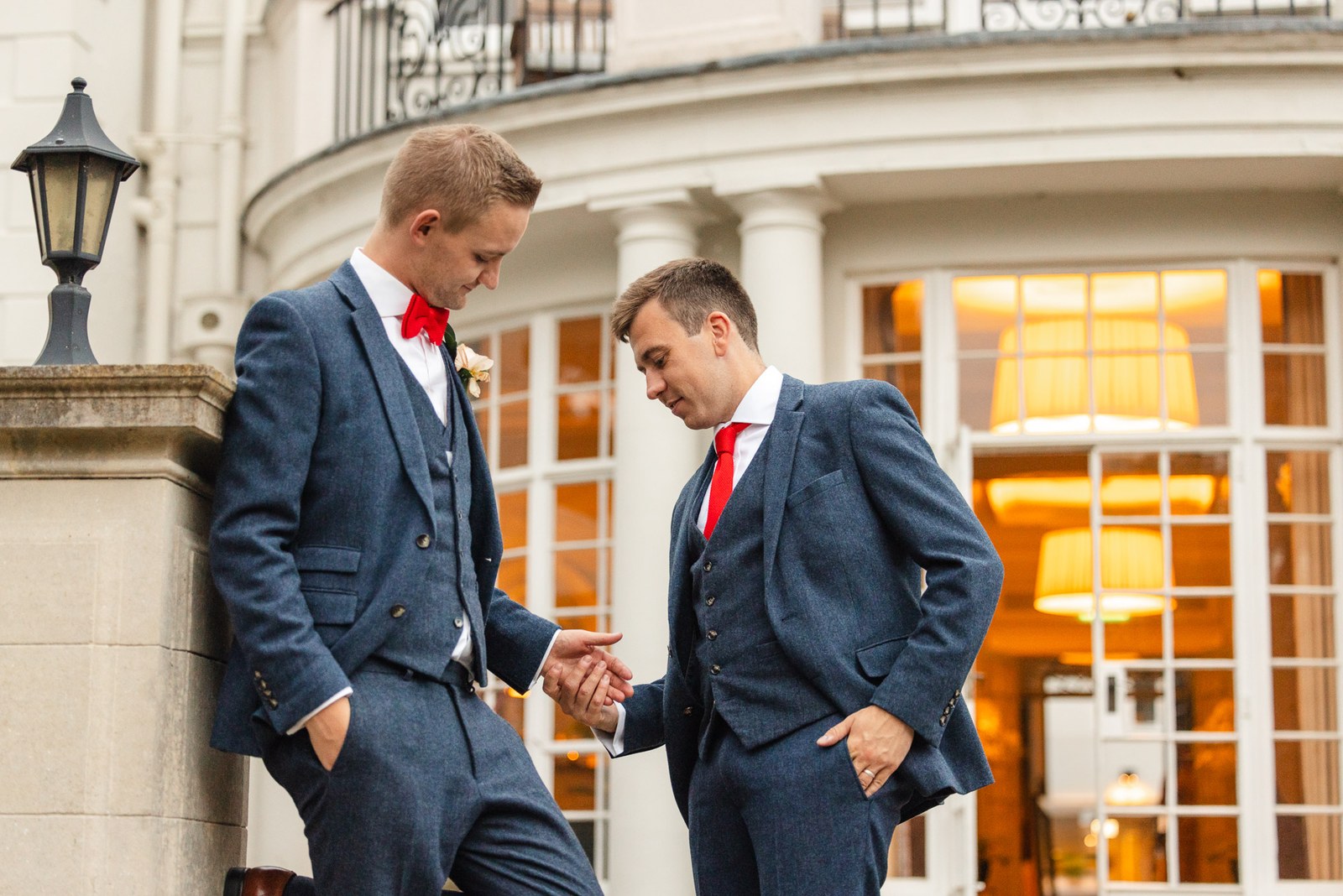 The two grooms leaning against the pillared facade of Gorse Hill Hotel at dusk