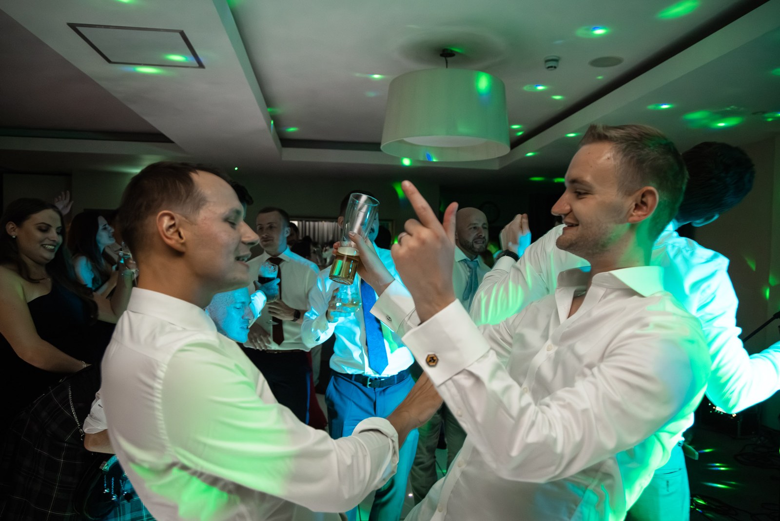 The grooms celebrating with drinks under green lights on the dance floor