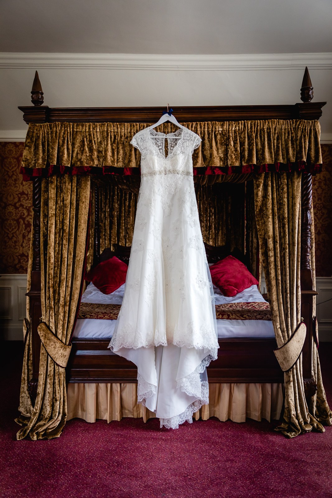 The lace wedding gown hanging on a carved gold-draped four-poster bed at Grim's Dyke Hotel