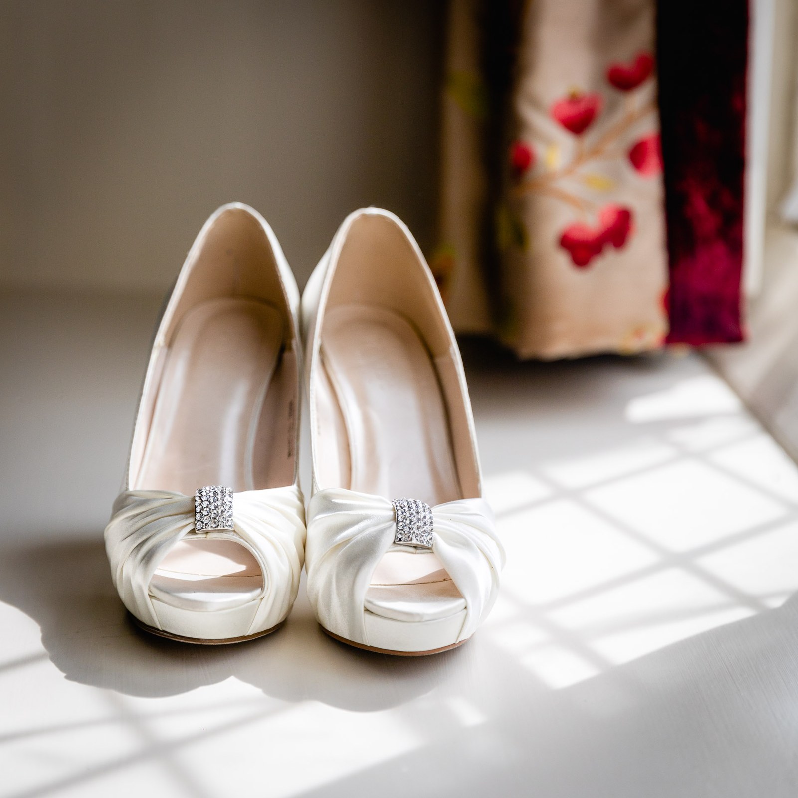 A pair of ivory satin peep-toe heels with diamante detail in the sunlight