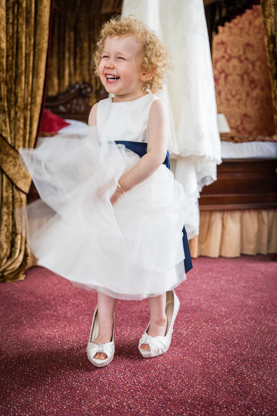 A flower girl in white with a navy sash twirling and laughing by the four-poster bed