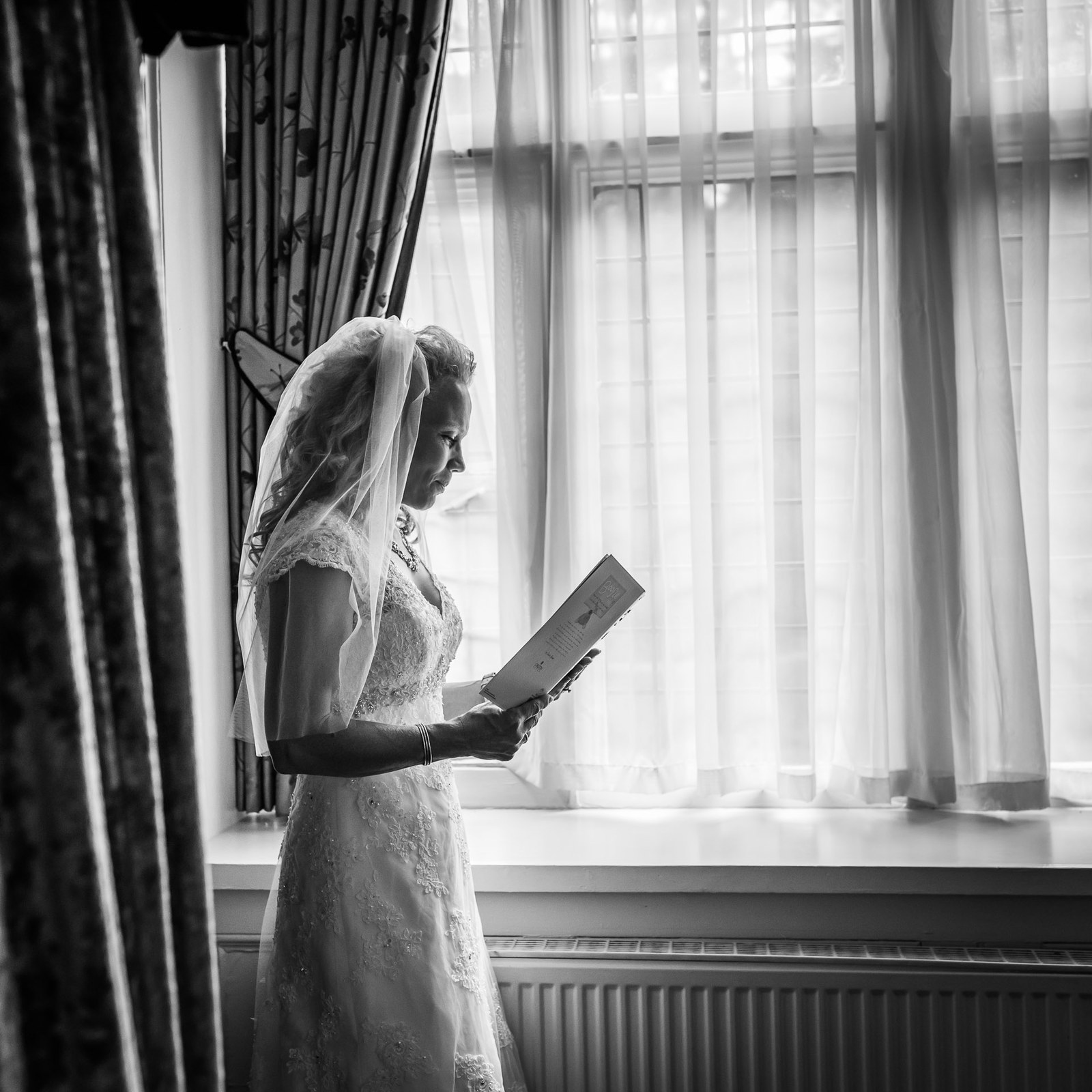 Black-and-white of the bride reading a card by a tall window