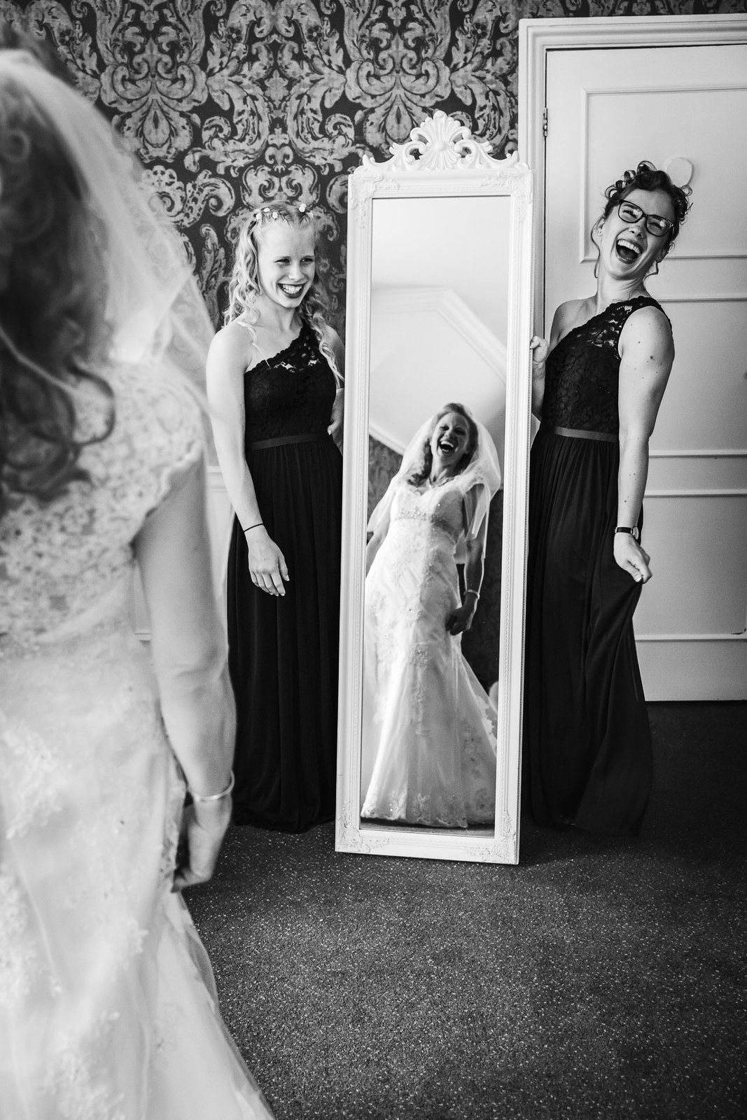 Black-and-white of the bride with her bridesmaids and her reflection in a tall mirror