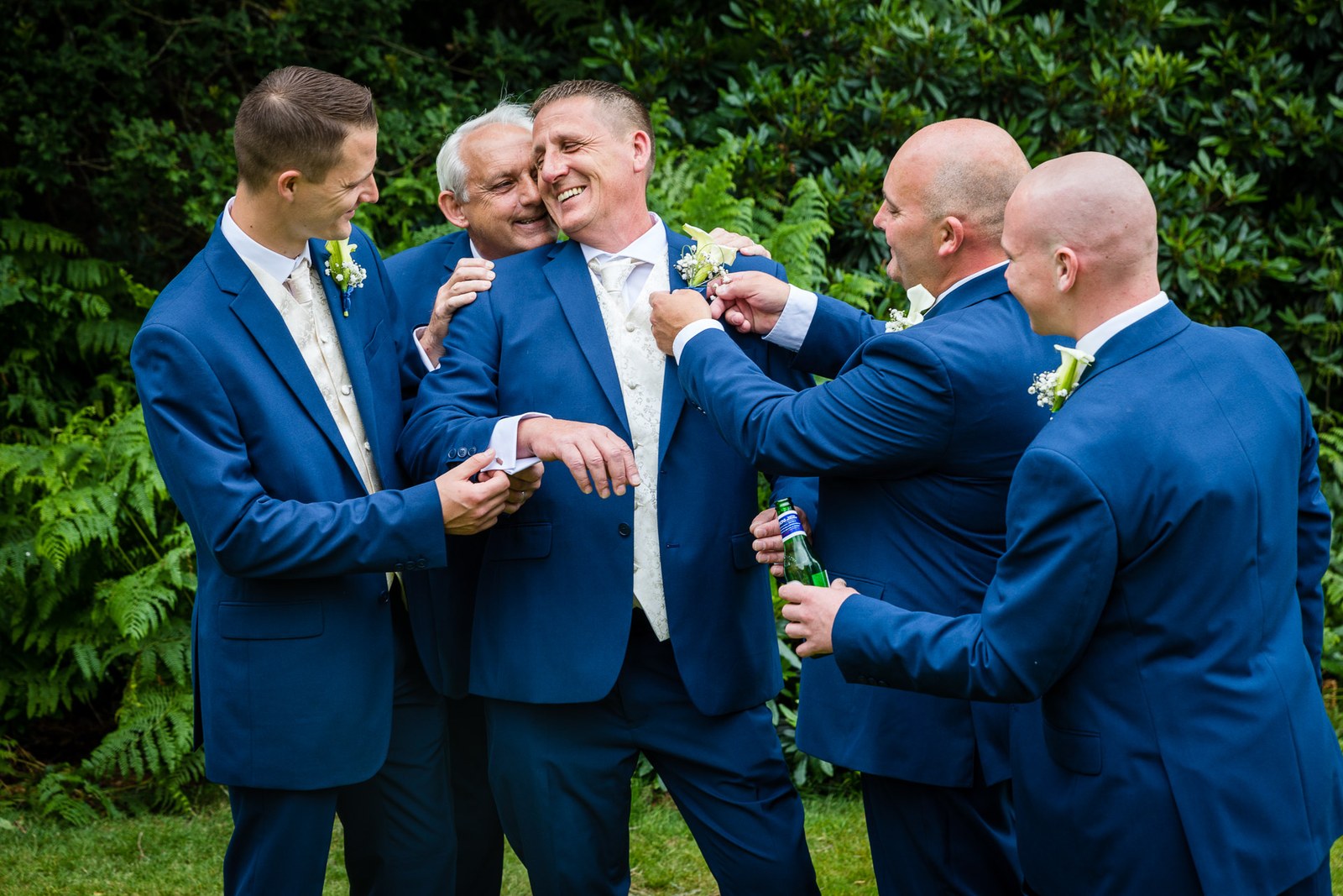 The groom and his groomsmen laughing together over buttonholes on the lawn