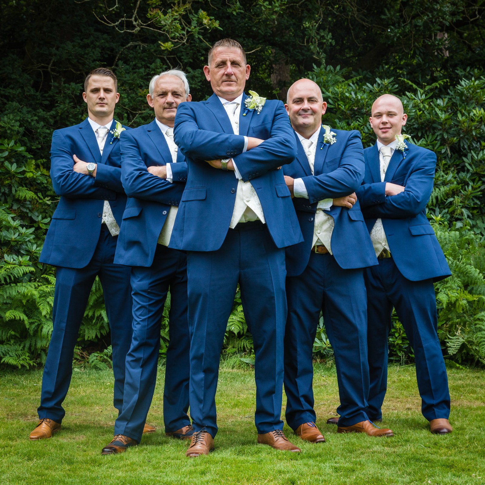 The groom and groomsmen posing with folded arms against leafy greenery