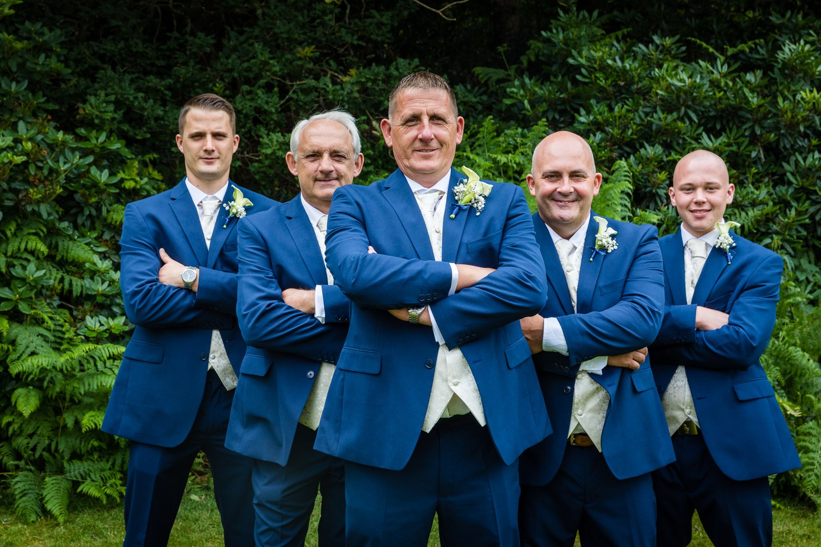 The groom and groomsmen smiling together in their blue suits on the lawn