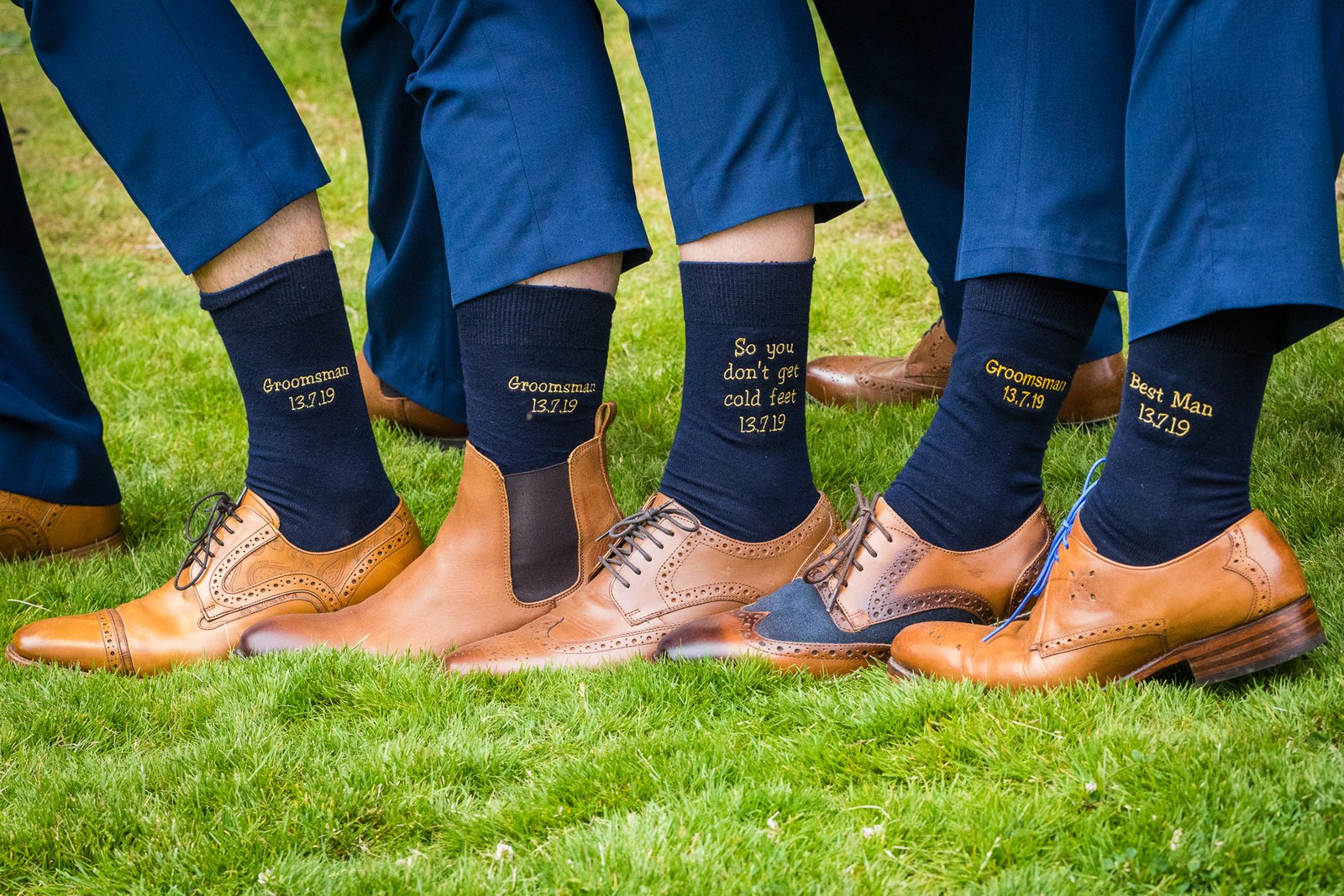 The groomsmen's navy socks embroidered with their roles above tan brogues on the grass