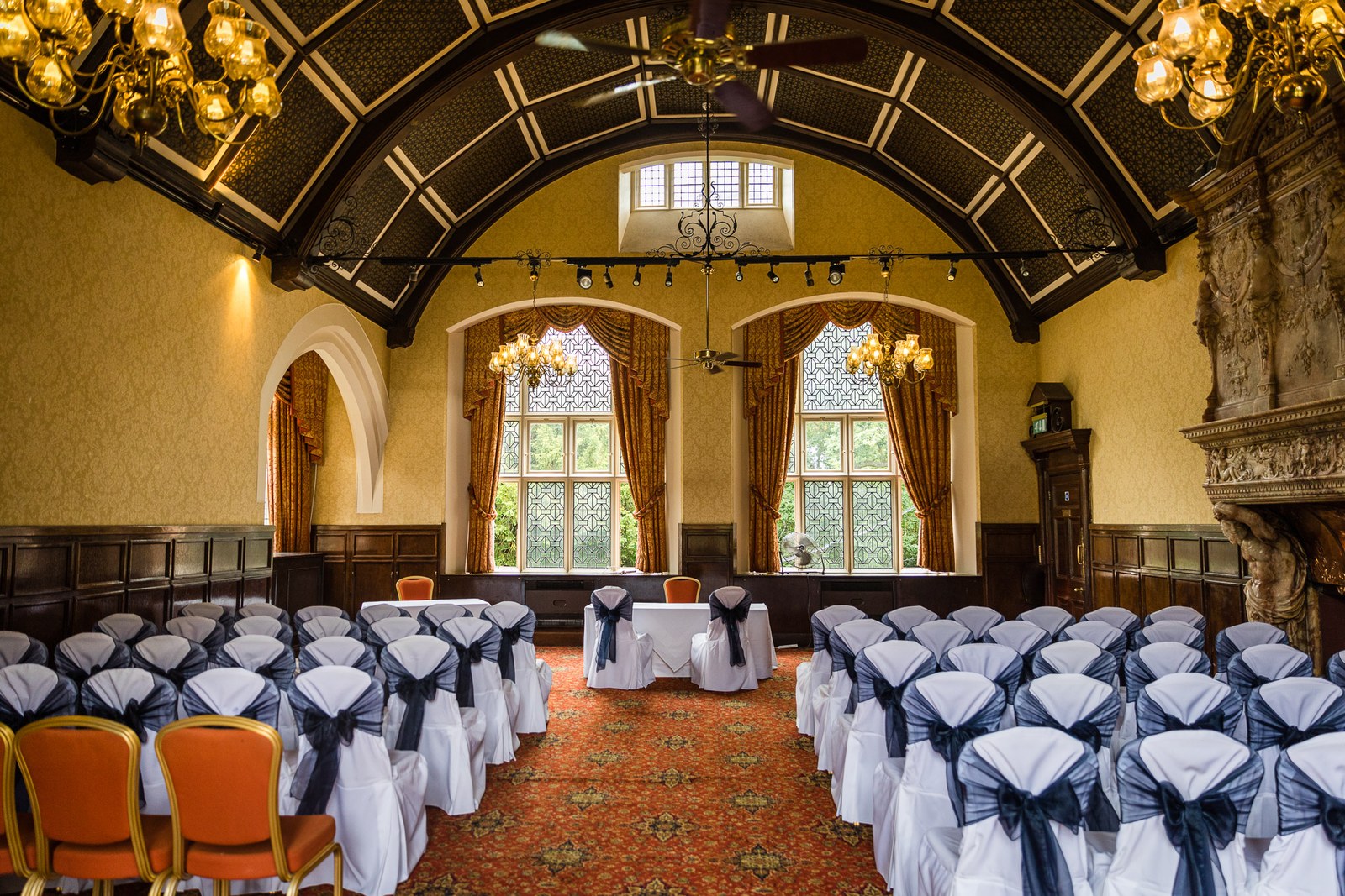 The panelled ceremony hall at Grim's Dyke Hotel set with navy-sashed chairs beneath a painted vaulted ceiling