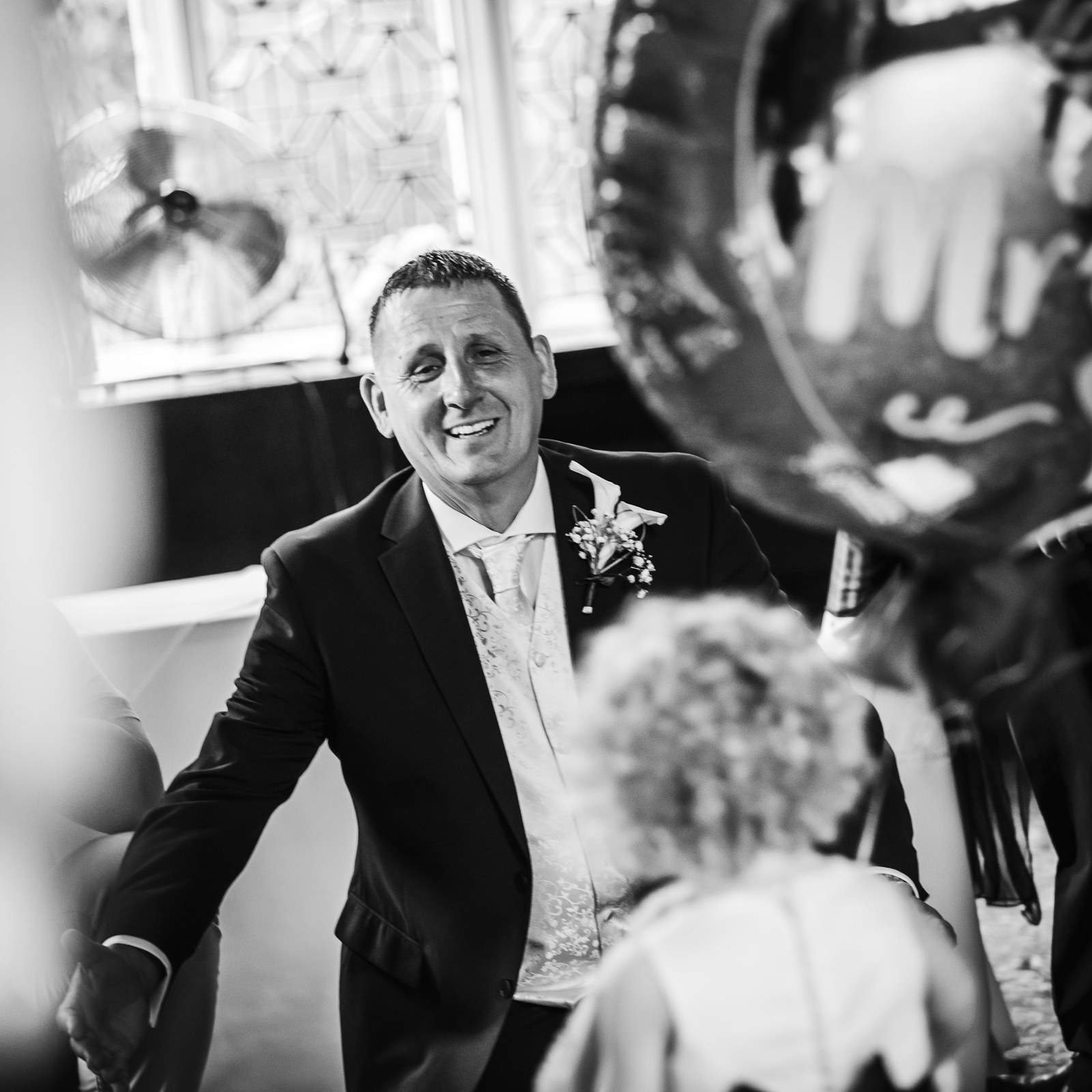 Black-and-white of the groom greeting a seated guest, a balloon behind