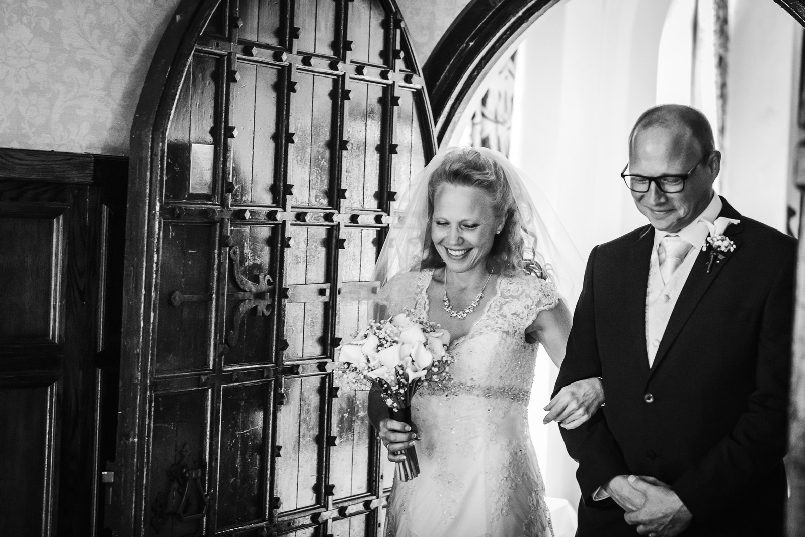 The bride arriving on her father's arm through the grand studded oak door at Grim's Dyke Hotel