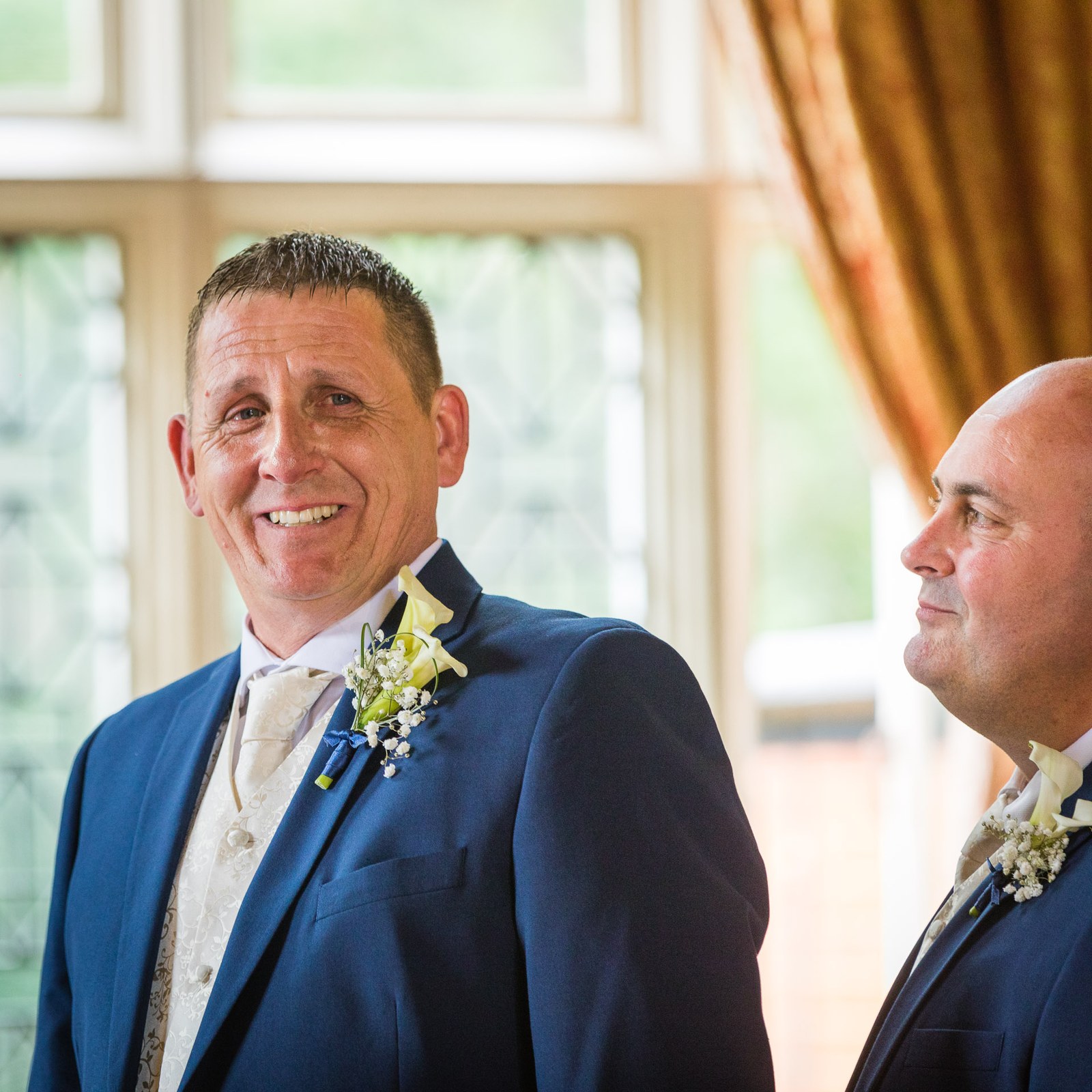 The groom smiling beside his best man, the leaded windows of Grim's Dyke Hotel behind