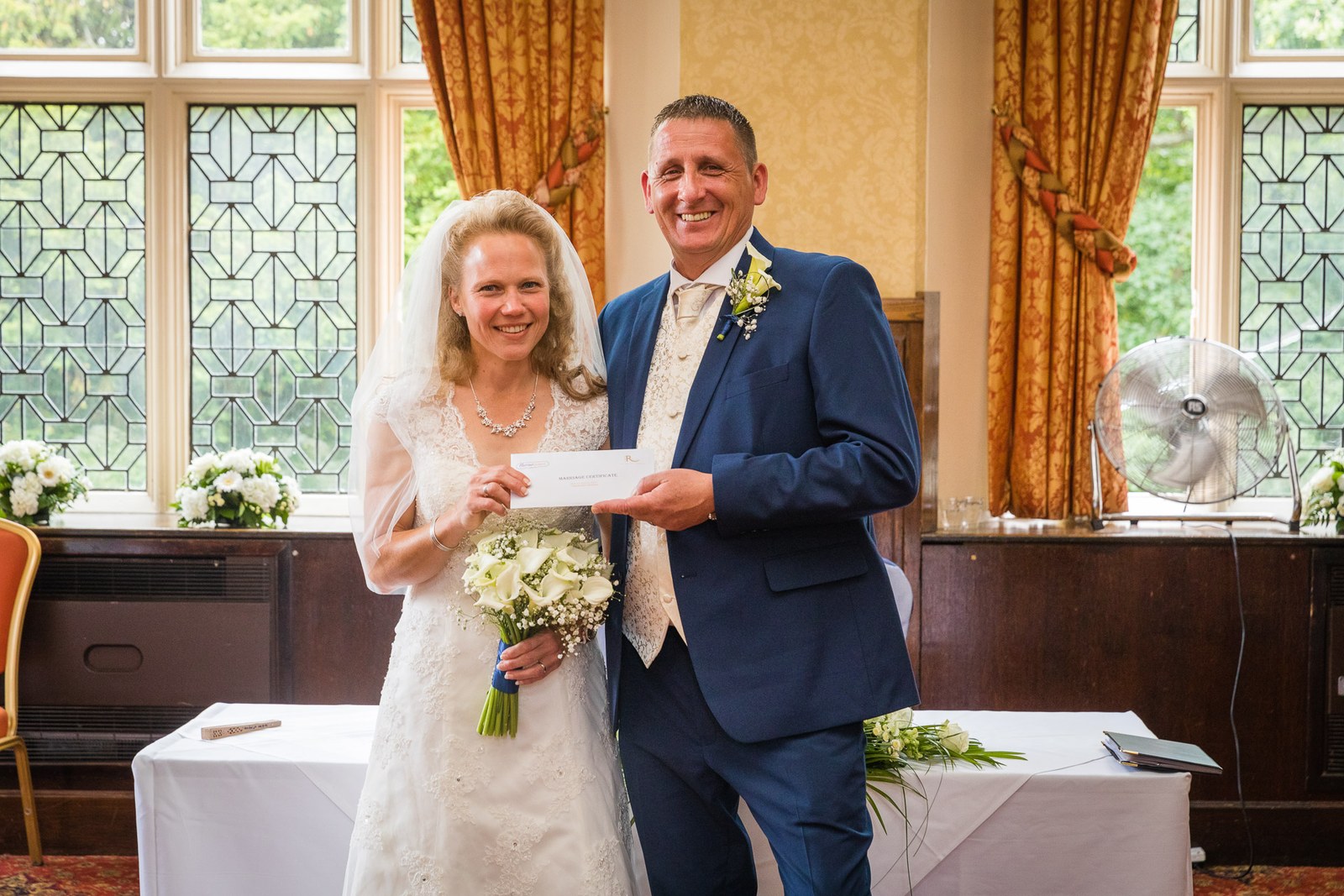 The newlyweds proudly holding up their marriage certificate by the leaded windows