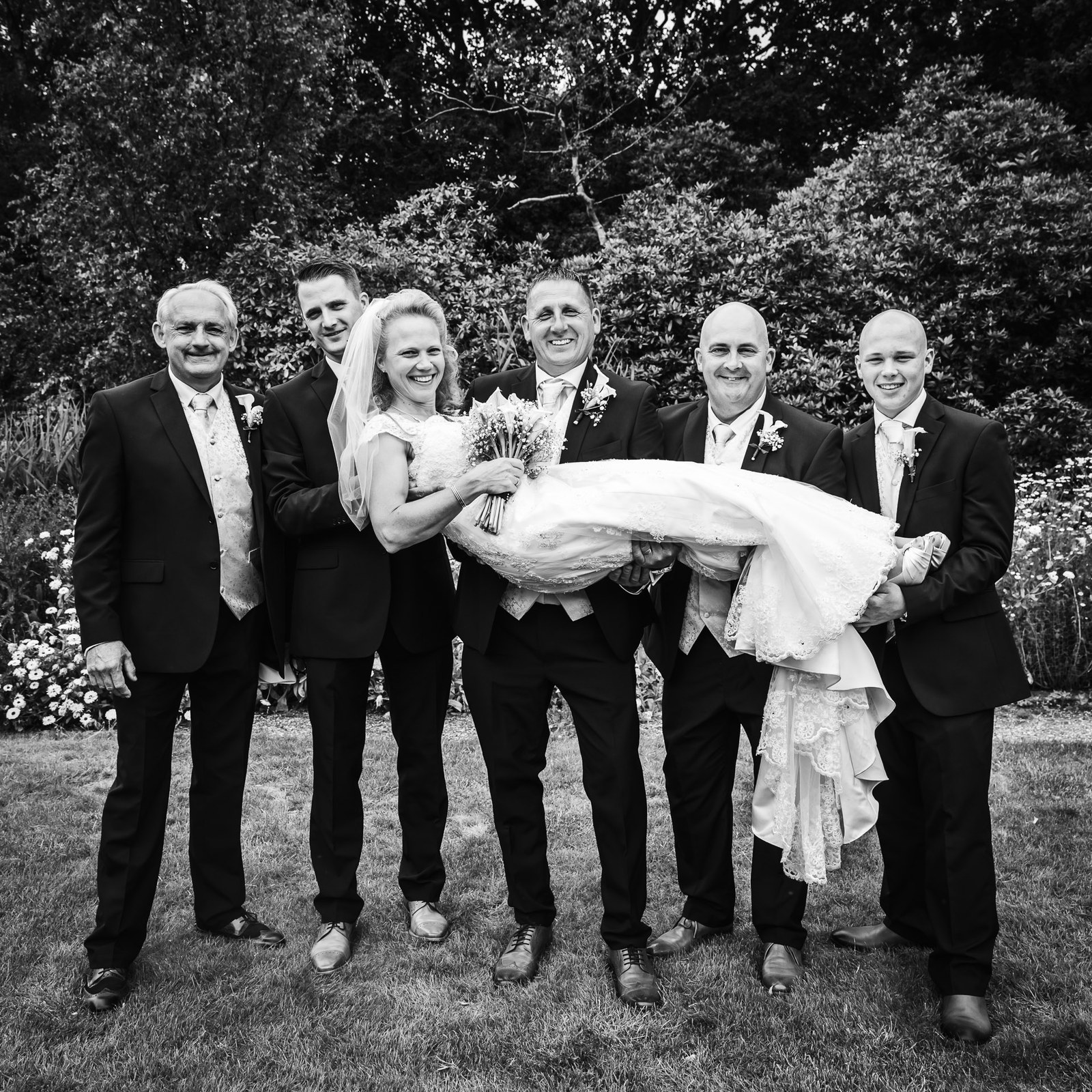 Black-and-white of a group of men carrying the laughing bride aloft on the lawn