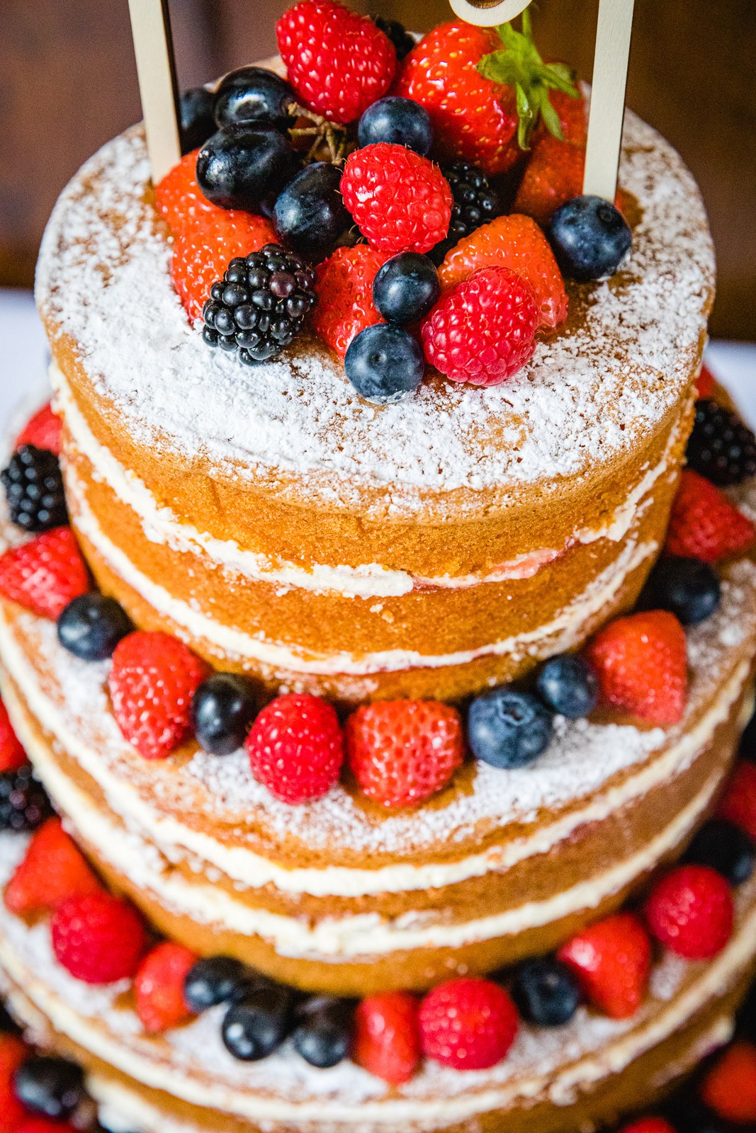 A naked sponge cake topped with fresh berries and dusted with icing sugar