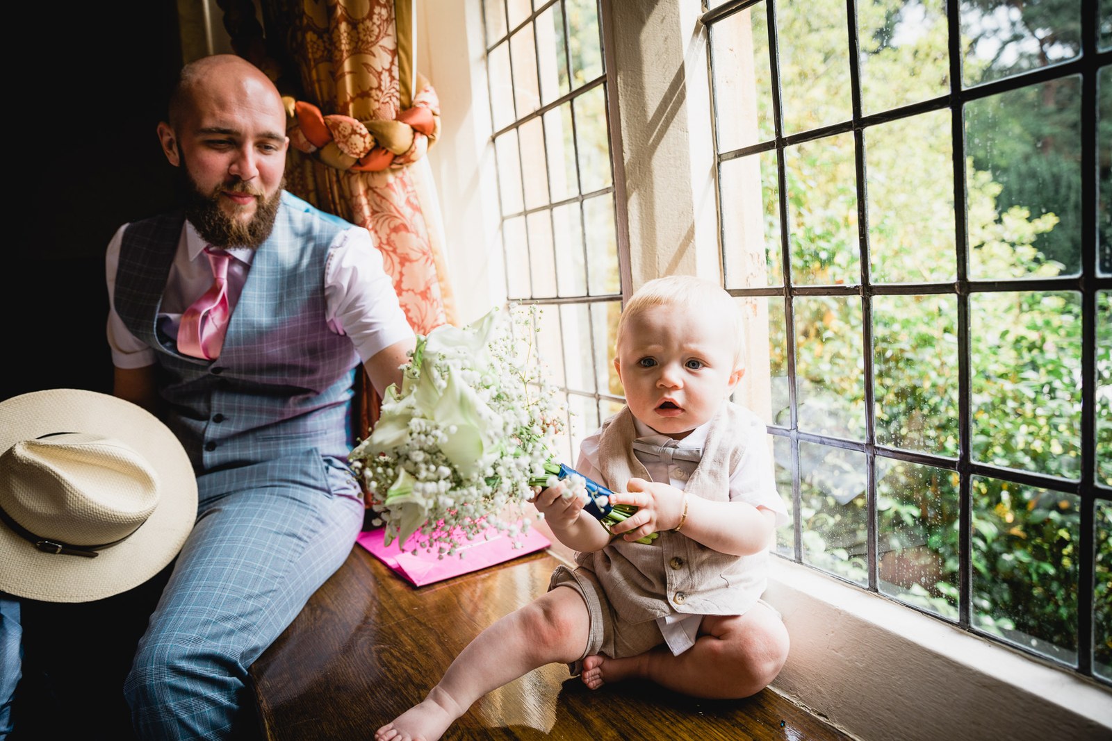 A guest and a baby on a window seat by the leaded windows, a straw hat beside them