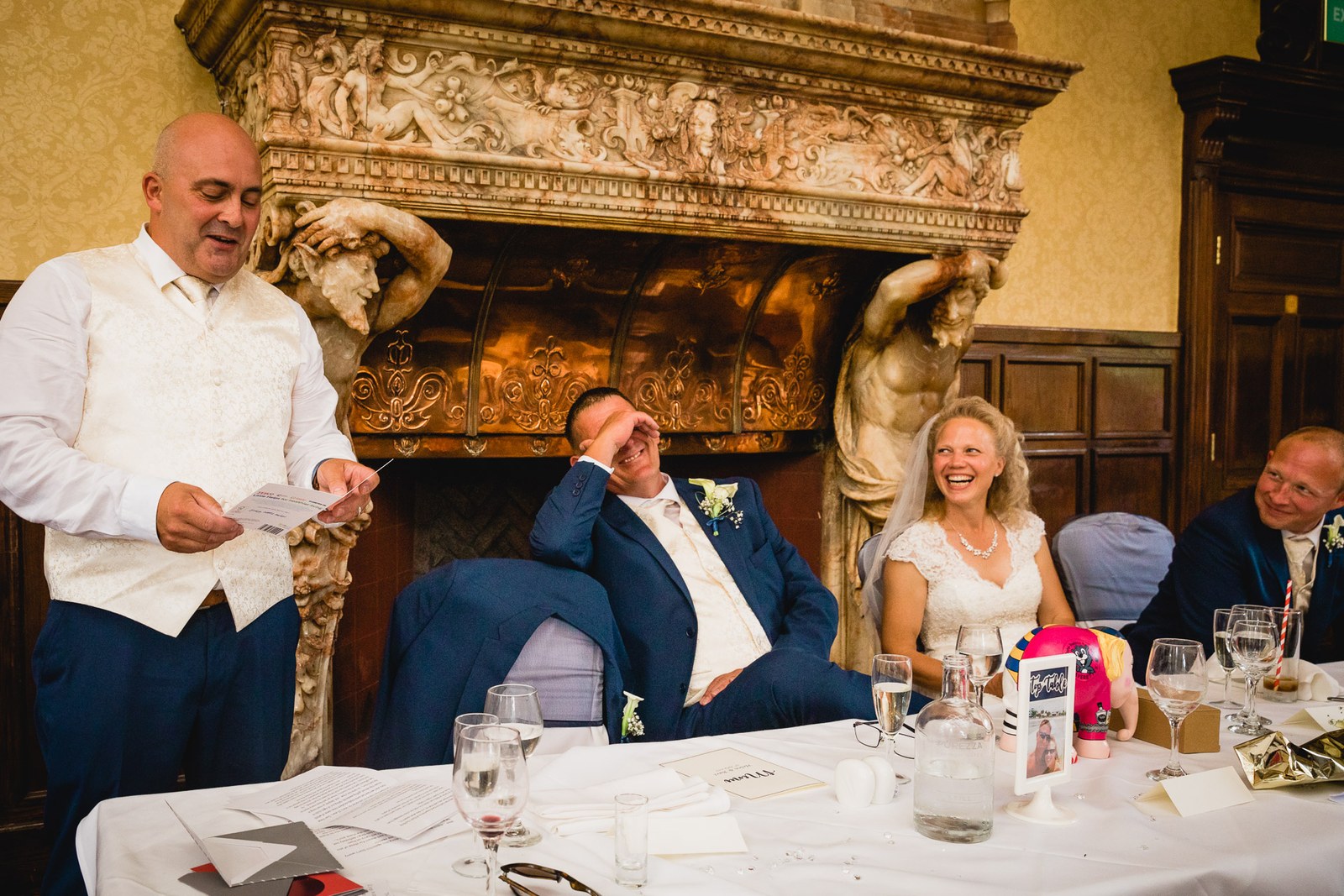 The best man giving his speech by the carved fireplace at Grim's Dyke Hotel as the groom laughs