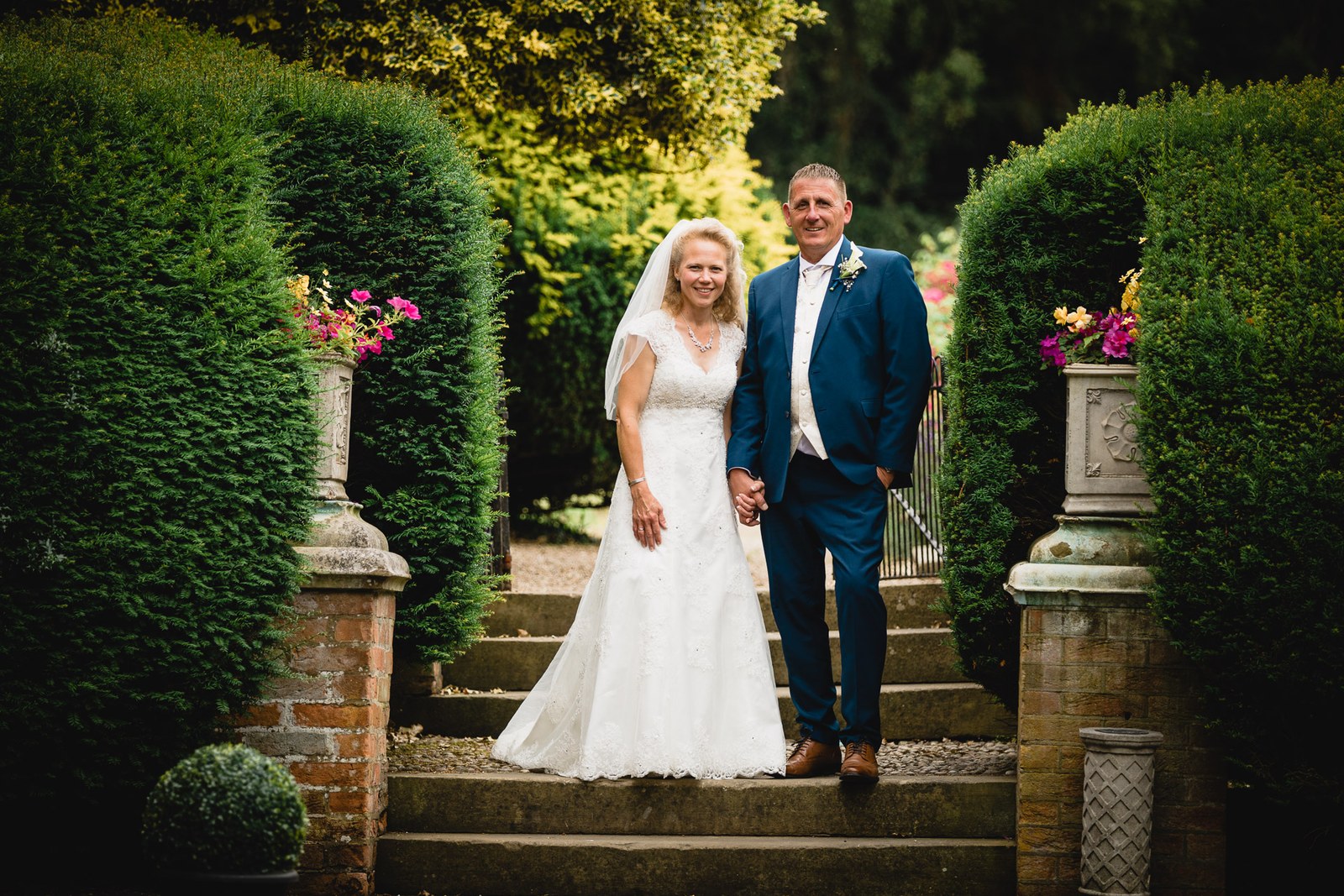 The couple on the stone garden steps between towering topiary at Grim's Dyke Hotel