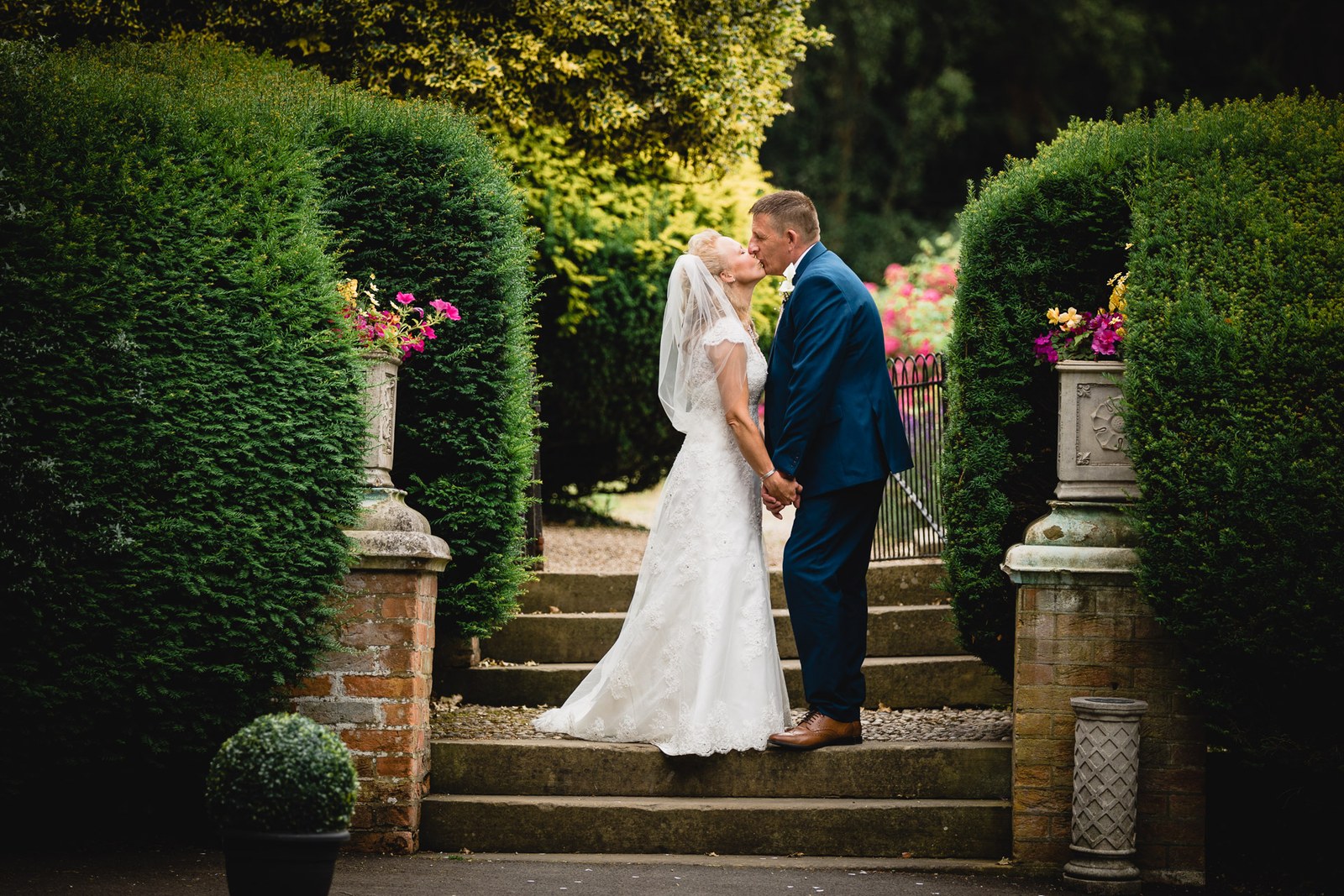 The couple kissing on the garden steps framed by clipped yews at Grim's Dyke Hotel