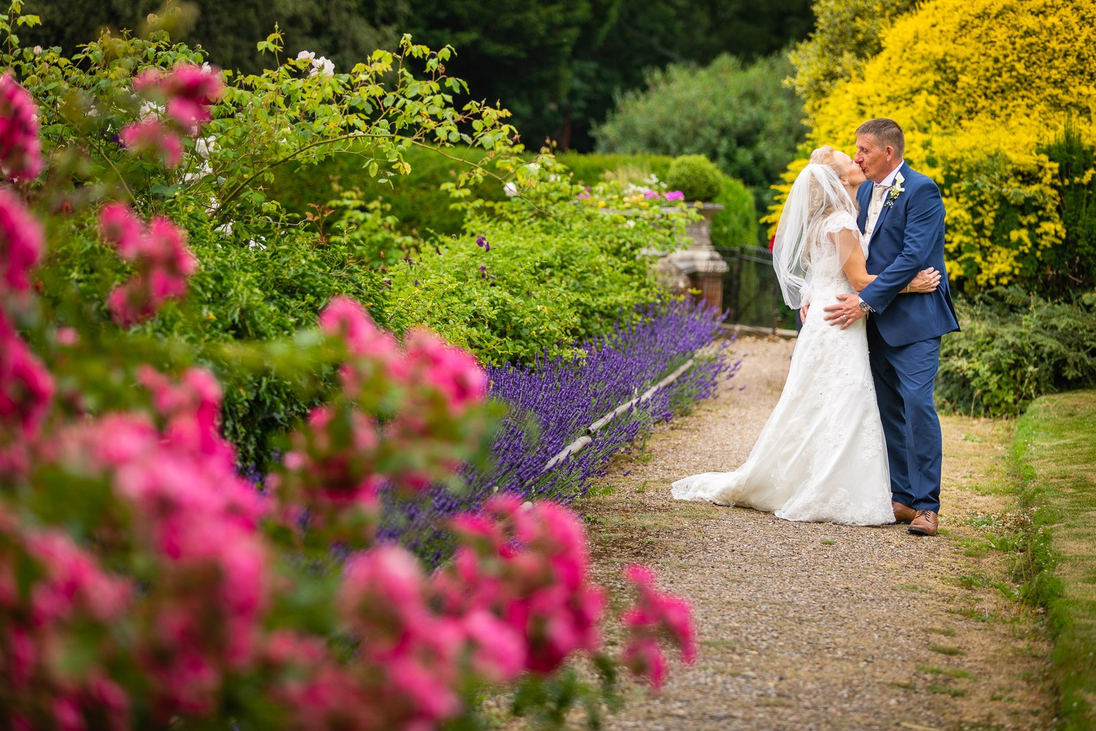 The couple embracing on a garden path of roses and lavender at Grim's Dyke Hotel