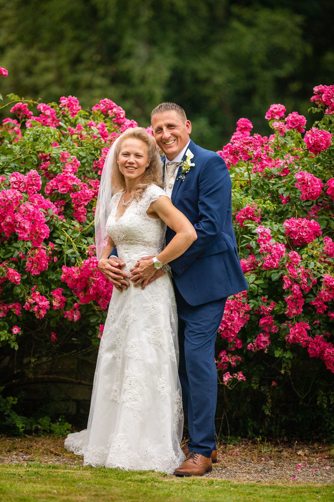 The couple embracing before a mass of pink roses, the bride laughing