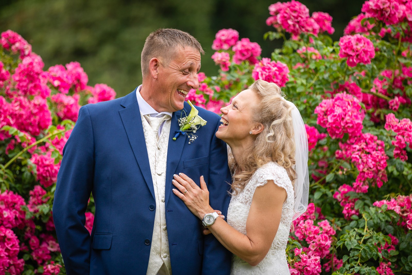 The couple laughing together, the bride's hand on the groom's chest by the roses