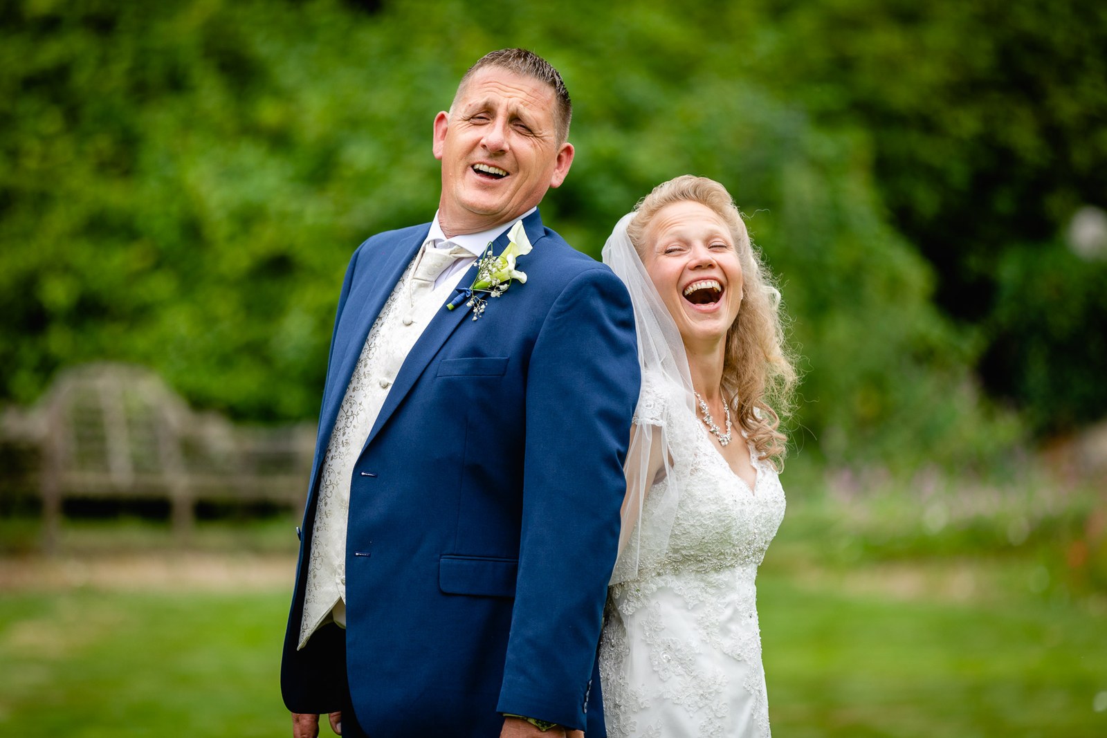 The couple laughing together on the lawn, a garden bench behind at Grim's Dyke Hotel