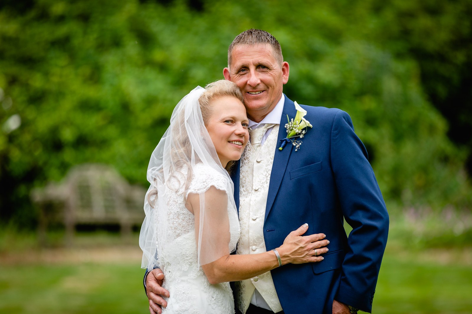 The couple embracing on the lawn at Grim's Dyke Hotel, garden benches behind