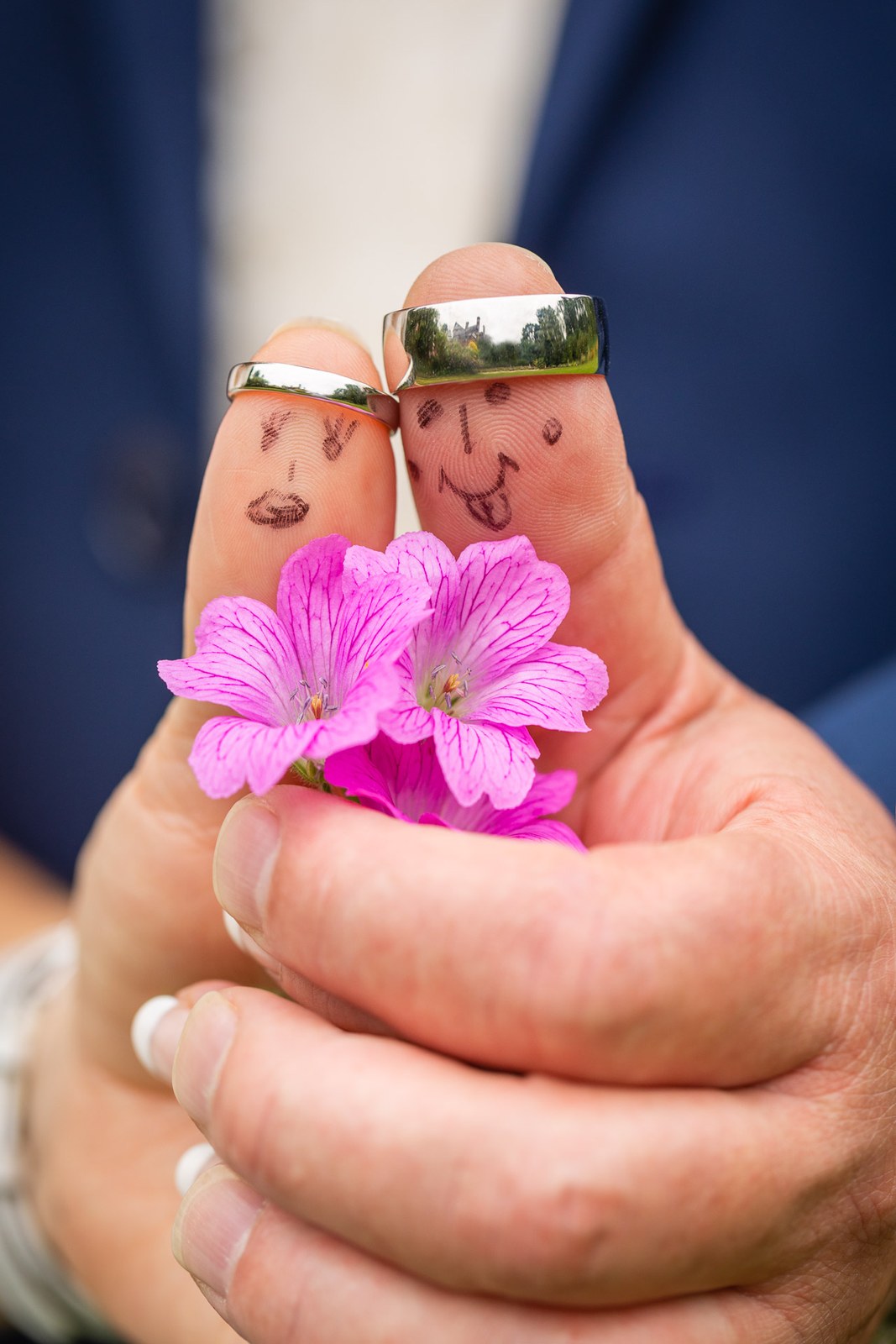 Close-up of the couple's ringed fingers with tiny faces drawn on, holding pink flowers